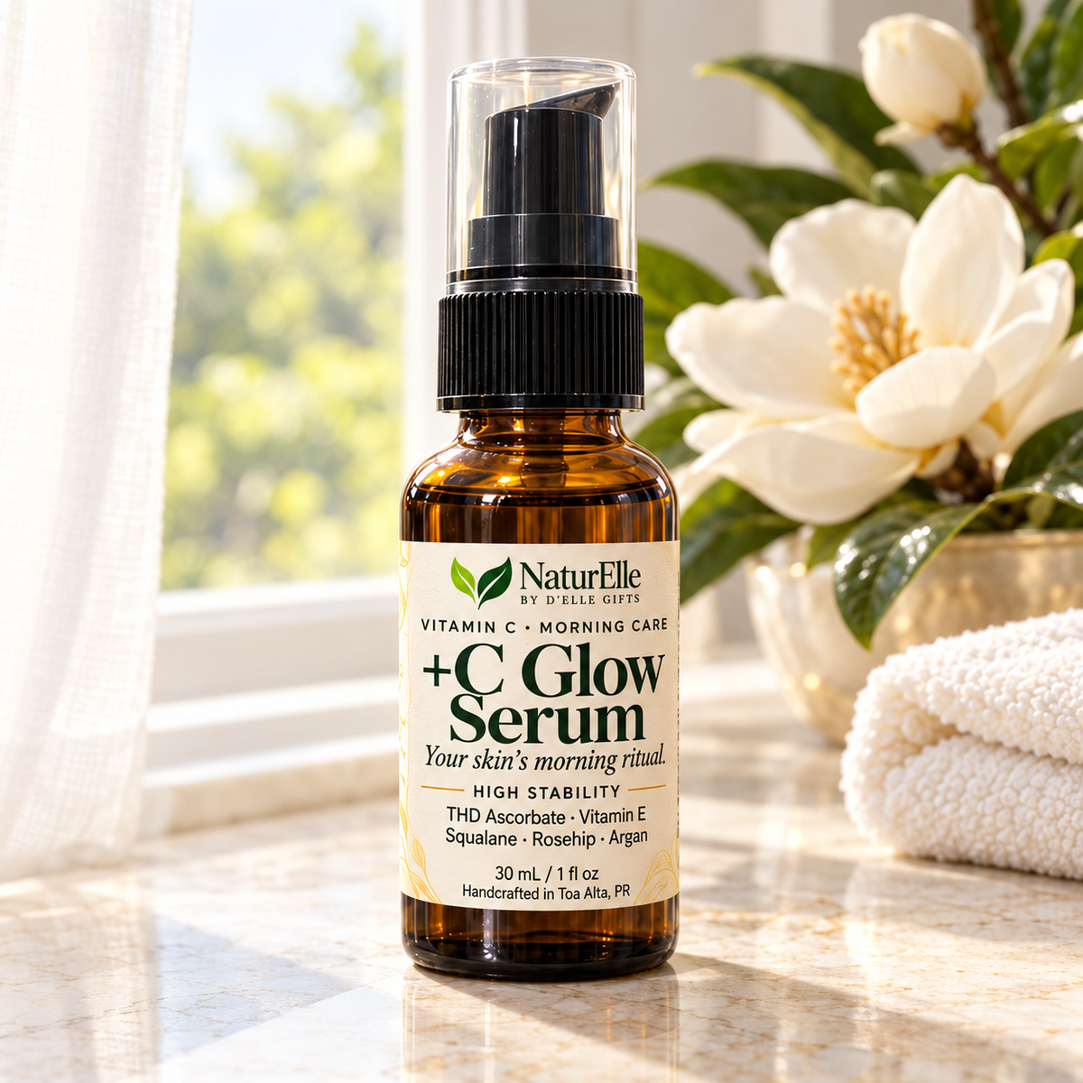 A 30 mL amber glass bottle of NaturElle +C Glow Serum with a black pump and clear cap, set on a marble surface with a white towel and white flowers in the background.
