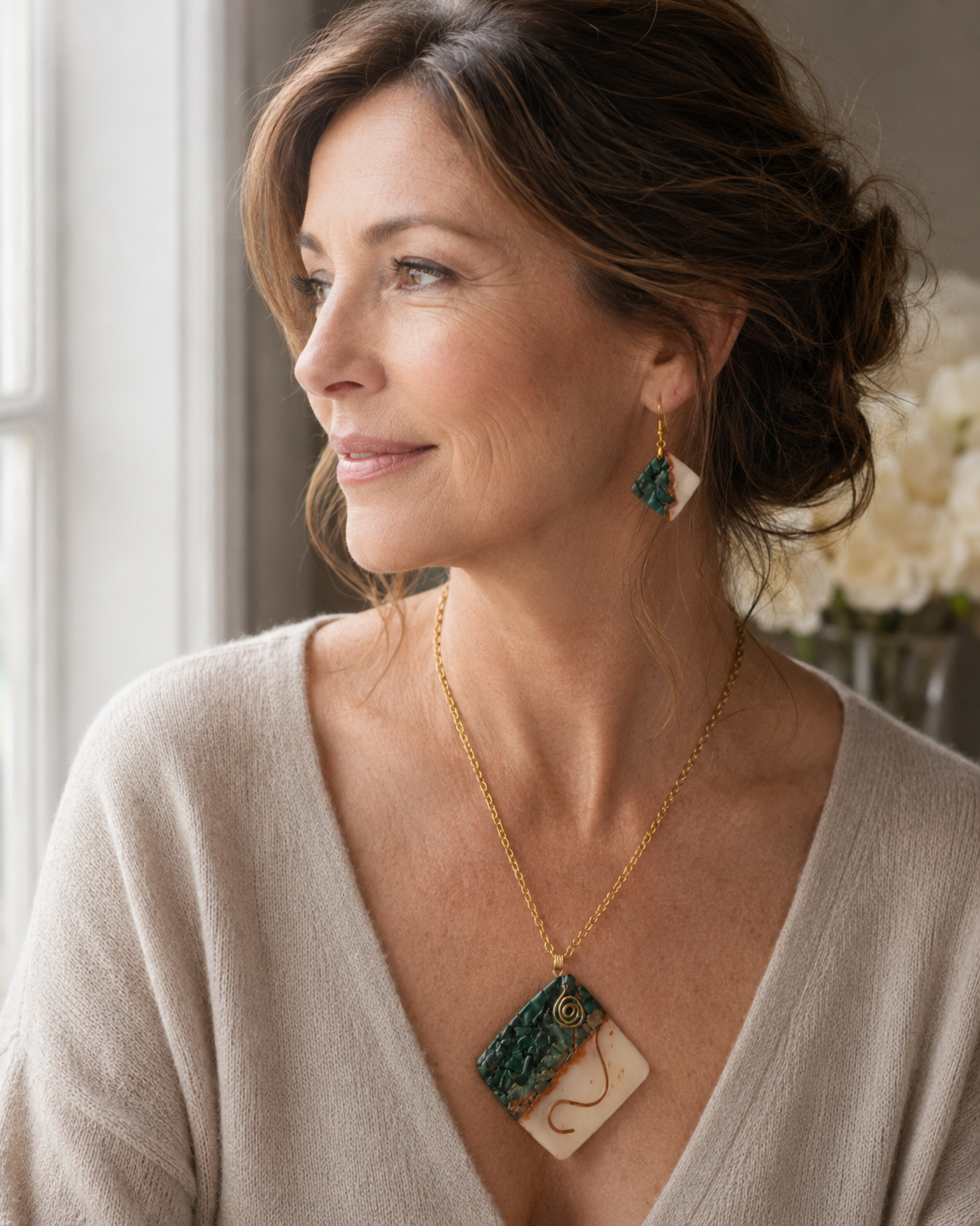 Una mujer luce un collar de cadena de oro con un colgante rectangular con un estampado jaspeado en verde y crema, y ​​un pendiente colgante a juego, en un ambiente interior con iluminación tenue - D'Elle Gifts