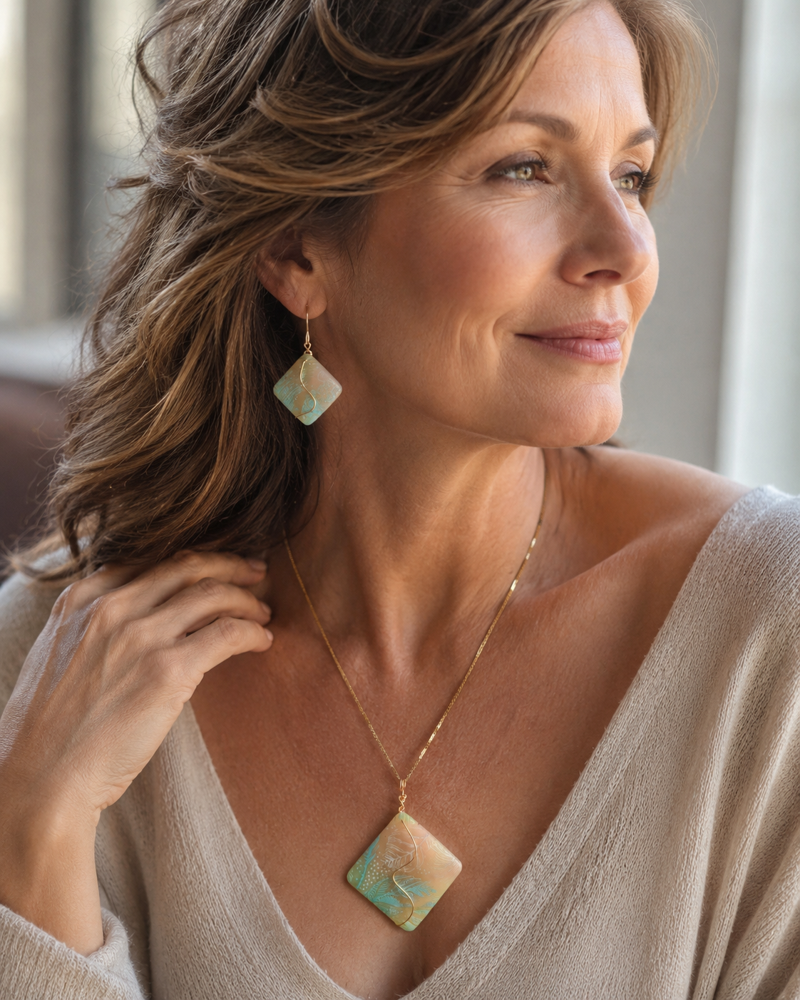 Una mujer luce un collar de oro con un colgante cuadrado y pendientes colgantes a juego, ambos con un diseño jaspeado en tonos crema, verde claro y turquesa, en una fotografía de estilo de vida tomada en primer plano - D'Elle Gifts