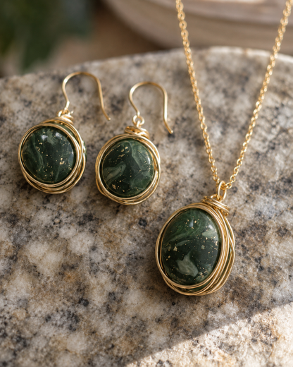 Conjunto de joyas de oro compuesto por un collar y unos pendientes colgantes a juego con cabujones ovalados de piedra verde jaspeada, presentados sobre una superficie de granito texturizado - D'Elle Gifts
