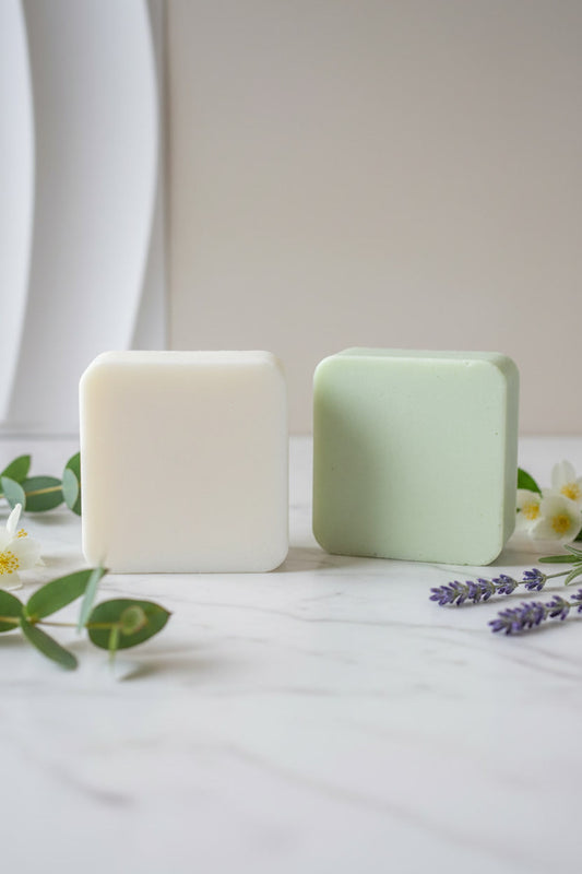 Dos pastillas de jabón, una blanca y otra verde, sobre una superficie clara con flores y hojas — NaturElle Puerto Rico