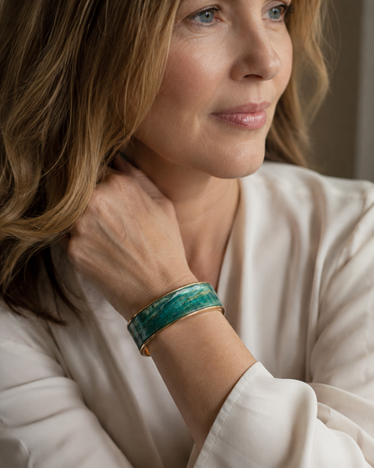 Primer plano de una mujer que luce una pulsera ancha y pulida de color turquesa y verde con bordes de metal dorado, combinada con una bata de satén color crema - D'Elle Gifts