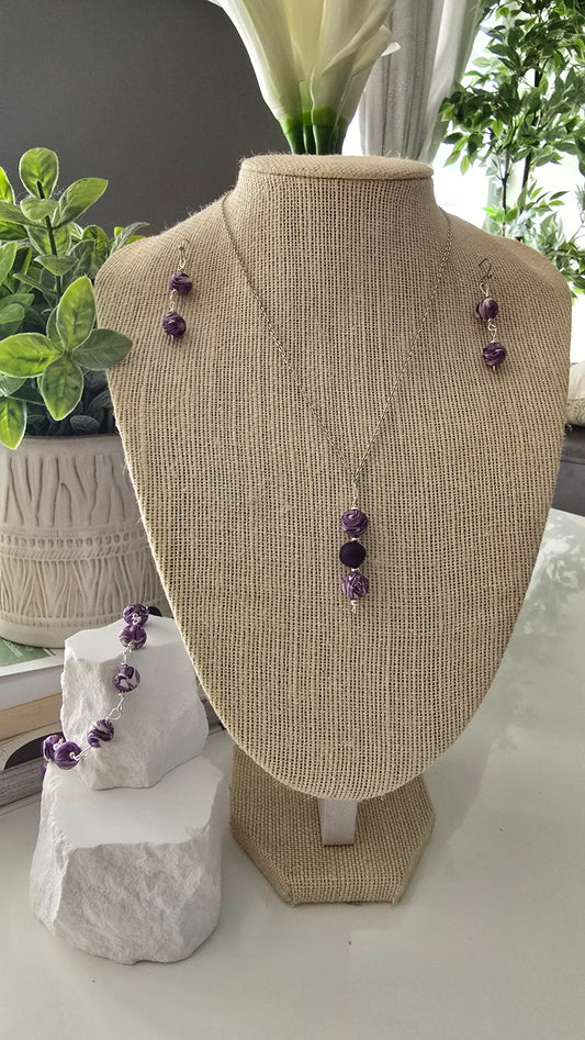 Pendientes, collar y pulsera morados y blancos expuestos en un busto de maniquí con fondo blanco.